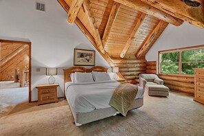 A bedroom with a sloped ceiling, a bed, a nightstand, a chair, and a dresser.