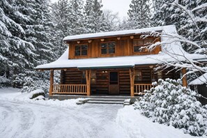 Una cabana de fusta amb un porxo, envoltada d'arbres coberts de neu.
