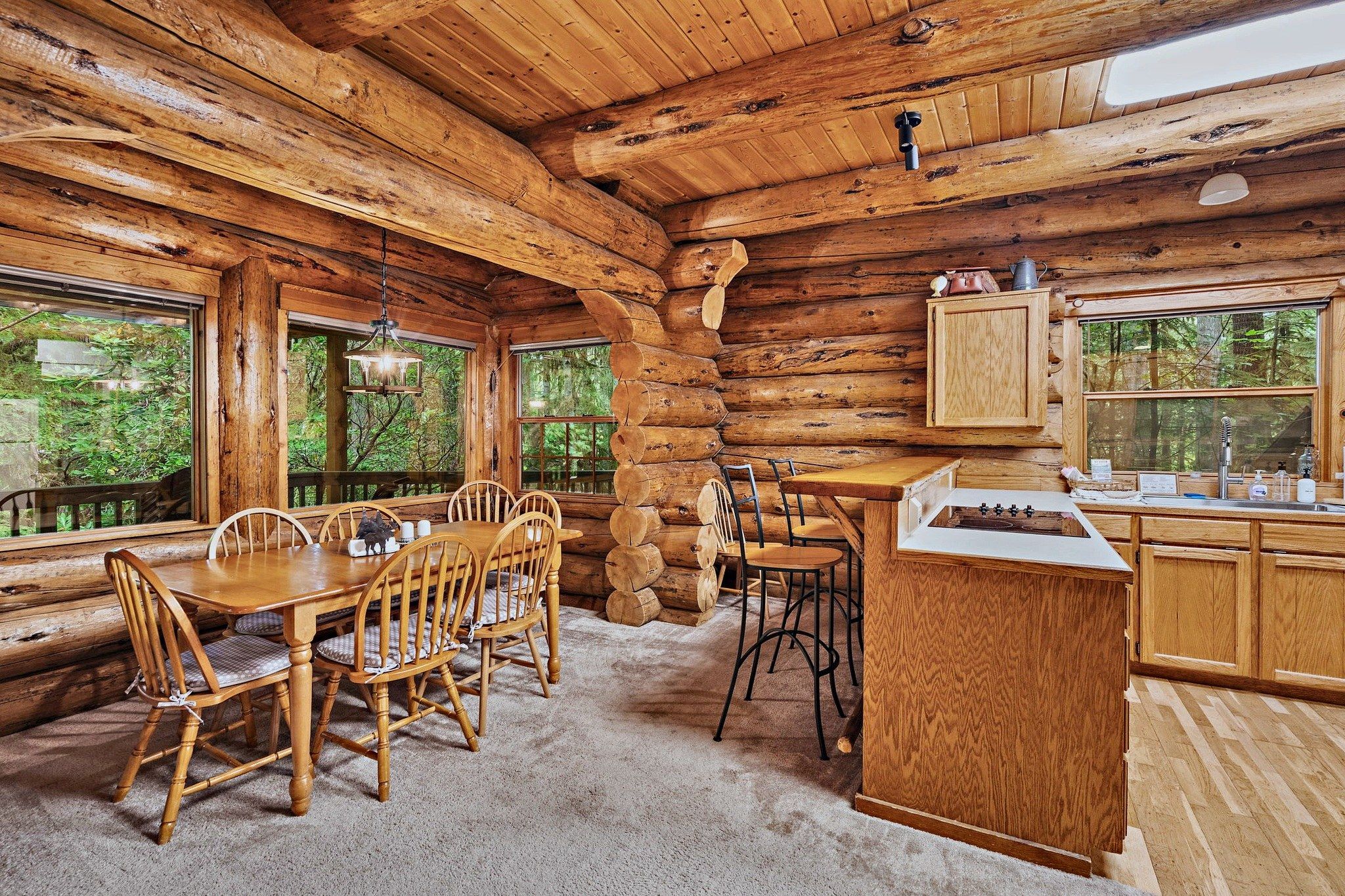 Ein Holzblockhaus-Interieur mit Essbereich, Küche und großen Fenstern mit Blick auf den Wald.