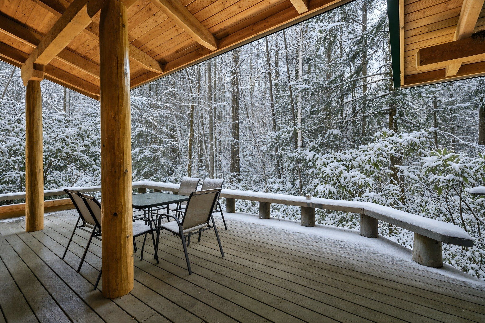 A wooden deck with a table and chairs, overlooking a snowy forest.