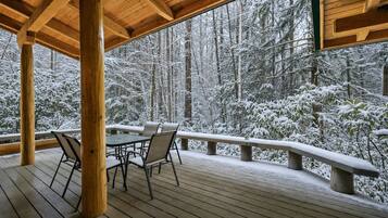 A wooden deck with a table and chairs, overlooking a snowy forest.