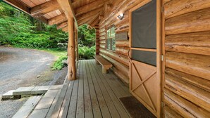 A wooden cabin with a porch, a bench, and a door with a window.