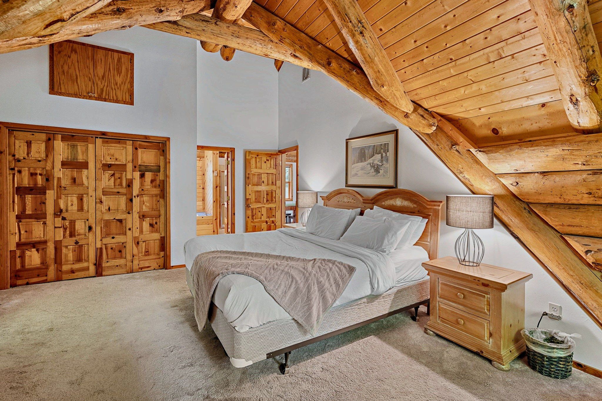 Une chambre avec un plafond en pente, des meubles en bois, un lit avec des oreillers, une table de chevet et un tableau encadré au mur.