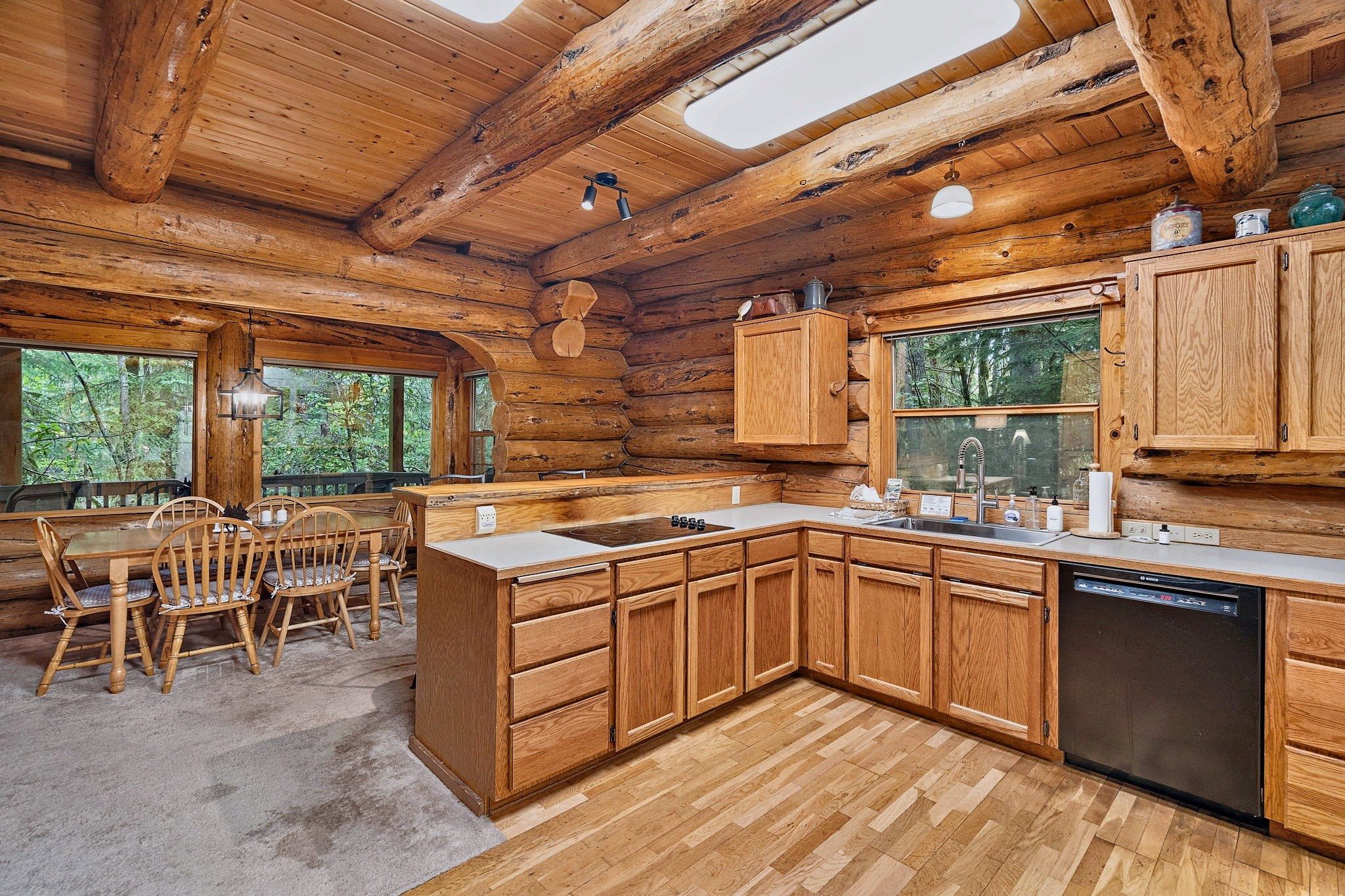 Interior de una cabaña de madera con cocina, comedor y ventanas amplias.