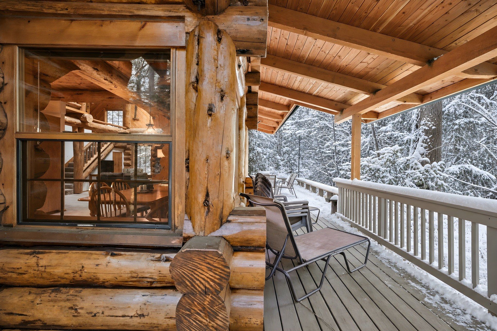 A wooden cabin with a covered porch, a dining area with chairs, and a view of snow-covered trees.