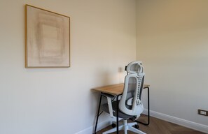 Ein Zimmer mit Schreibtisch, Stuhl, gerahmtem Bild an der Wand und einer Steckdose.