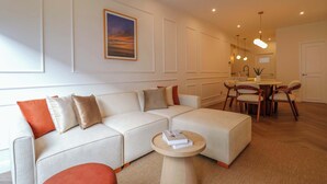 A modern living room with a sectional sofa, a round coffee table, and a dining area with wooden chairs and a table. - w* | Designer 2BR Stay w/ Balcony in Miraflores (Lima)