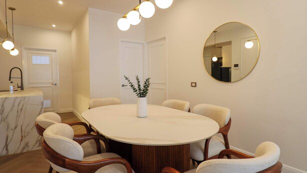 A dining area with a round table, six chairs, a vase with plants, a round mirror, and pendant lighting. - w* | Designer 2BR Stay w/ Balcony in Miraflores (Lima)