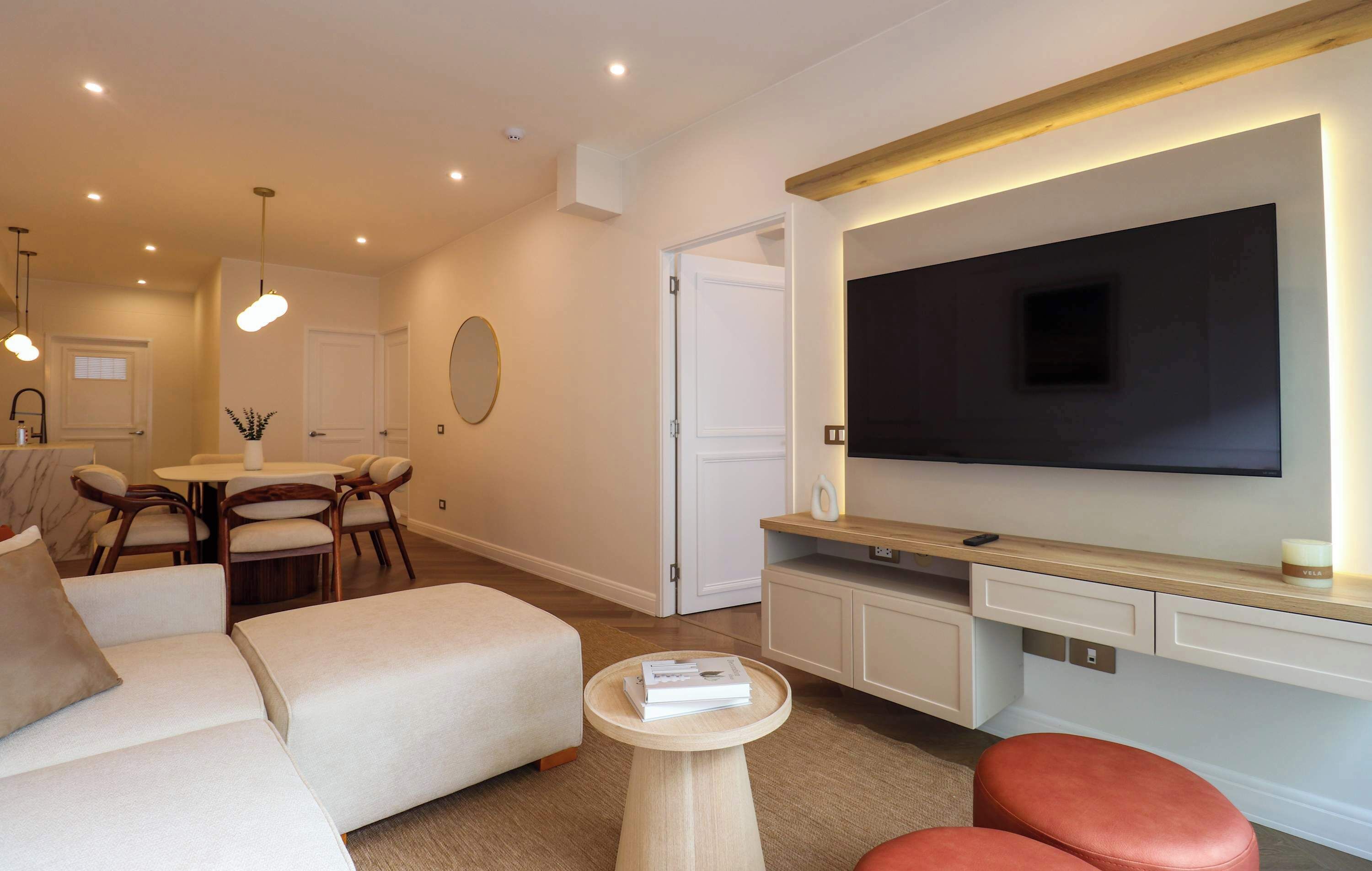 A modern living room with a flat-screen TV, a sofa, a coffee table, and a dining area with chairs and a table.