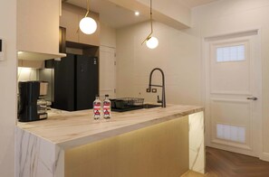 A modern kitchen with a marble countertop, a black refrigerator, a coffee maker, and two water bottles. - w* | Designer 2BR Stay w/ Balcony in Miraflores (Lima)