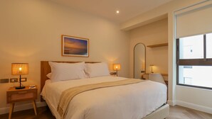 A hotel room with a large bed, two bedside lamps, a nightstand, a mirror, and a window. - w* | Designer 2BR Stay w/ Balcony in Miraflores (Lima)