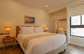Ein Hotelzimmer mit einem großen Bett, zwei Nachttischlampen, einem Nachttisch, einem Spiegel und einem Fenster.