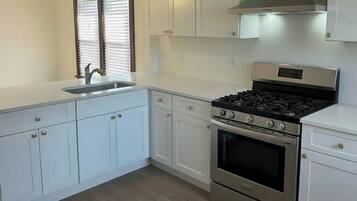A kitchen with white cabinets, a stainless steel stove, and a window with blinds.