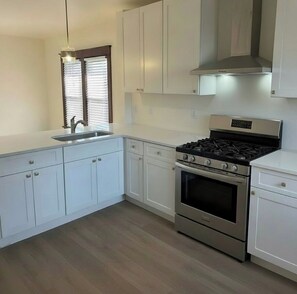 A kitchen with white cabinets, a stainless steel stove, and a window with blinds.