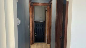 A narrow hallway with a wooden door at the end, white walls, and a light-colored floor.