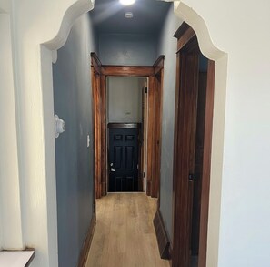 A narrow hallway with a wooden door at the end, white walls, and a light-colored floor. - Pet Friendly home, modern updates, minutes from Airport (St. Louis)