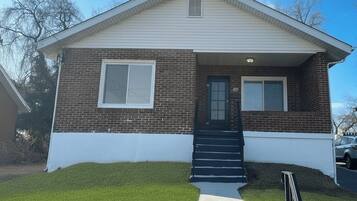 A single-story house with a brick facade, a front door, a small porch, and a clear sky.
