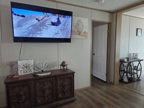 A room with a television mounted on the wall, a wooden cabinet with decorative items, and a door leading to another room. -  5-bedroom mobile home, 5 miles to Grand Lake. Close to Disney OK Rock Crawling  (Jay)