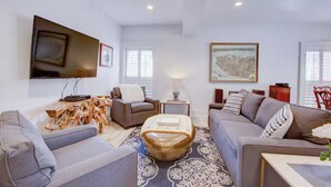 Ein modernes Wohnzimmer mit einem an der Wand montierten Flachbildfernseher, einer Sofagarnitur, einem Couchtisch und einem gemusterten Teppich.