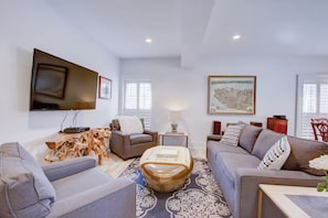 A modern living room with a flat-screen TV mounted on the wall, a sofa set, a coffee table, and a patterned rug. - Historic Charleston Right Outside Your Front Door (Charleston)