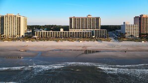 Un hotel frente a la playa con varios edificios altos, una playa de arena y un mar tranquilo.
