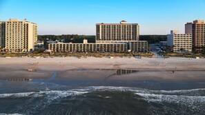 Um hotel à beira-mar com vários edifícios altos, uma praia de areia e um mar calmo.