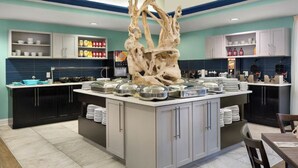 Una cocina moderna con una isla central, armarios negros y una escultura decorativa de un árbol.