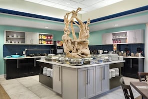 Uma cozinha moderna com uma ilha central, armários pretos e uma escultura decorativa de árvore.