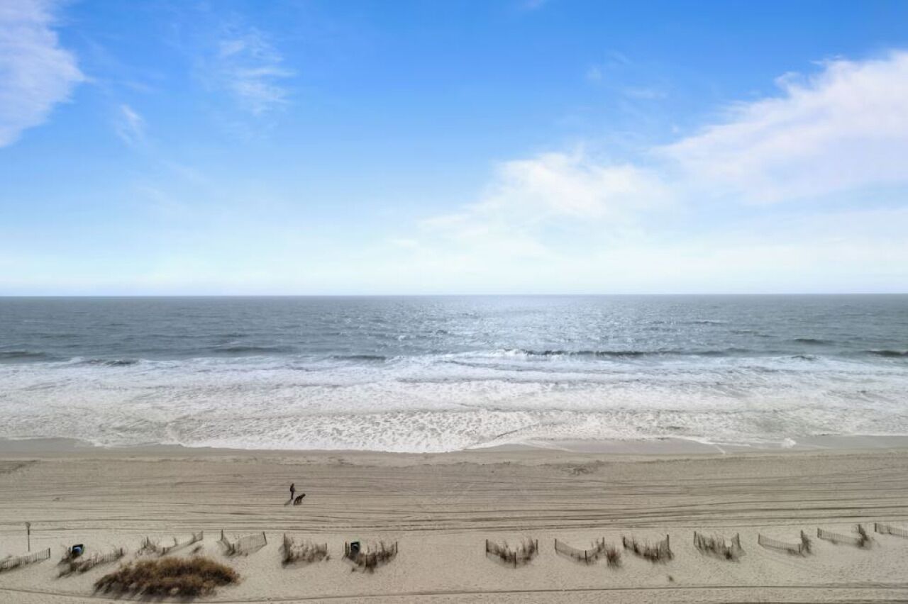 Une plage où une personne se promène le long du rivage, des vagues qui déferlent sur le sable et un ciel dégagé.
