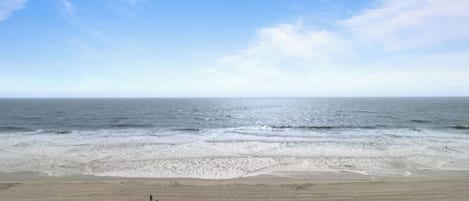 Une plage où une personne se promène le long du rivage, des vagues qui déferlent sur le sable et un ciel dégagé.