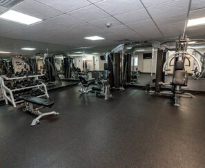 Ein Fitnessraum mit verschiedenen Trainingsgeräten, darunter Kurzhanteln, Bänke und Kraftgeräte.