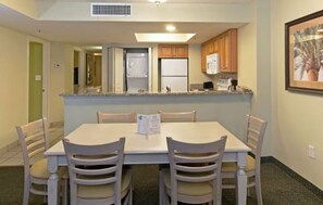 Un comedor con una mesa y sillas, una cocina con armarios y electrodomésticos, y un cuadro en la pared.