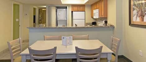 Un comedor con una mesa y sillas, una cocina con armarios y electrodomésticos, y un cuadro en la pared.