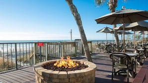 Eine Terrasse mit Feuerstelle, Sitzgelegenheiten und Blick auf den Strand.
