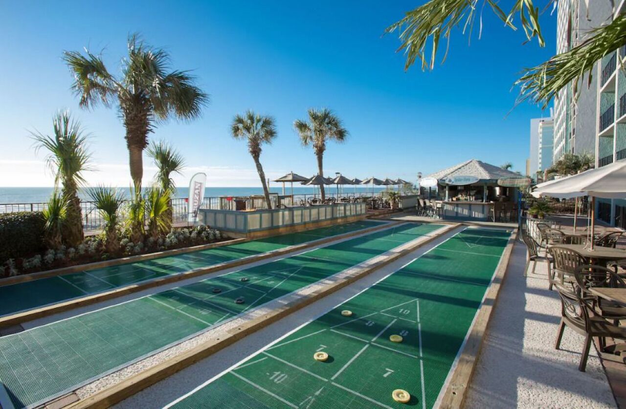 A pool table area with a view of the ocean, palm trees, and outdoor seating.