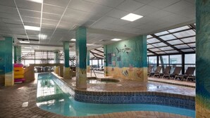 Una piscina interior con borde de azulejos, un mural de vida marina y una zona con tragaluces y sillones de descanso.