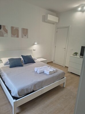 A neatly made bed with pillows, a bedside table, a wall-mounted air conditioner, and a closed door. - Not just a city - Torrette (Torrette)