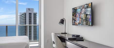 Habitación de hotel con balcón, escritorio, silla y televisor de pared mostrando carteles de películas.