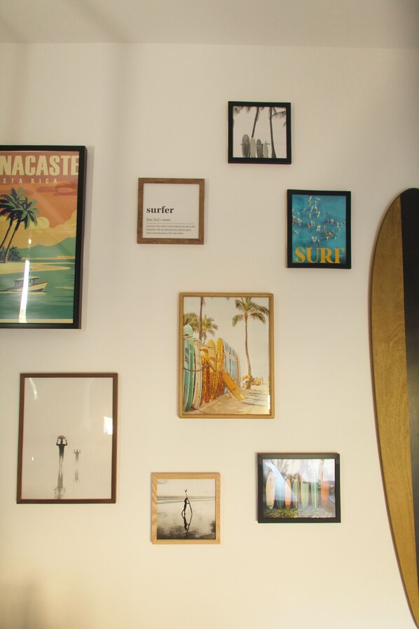 Una pared con diversos cuadros enmarcados, incluyendo una tabla de surf y una escena de playa.