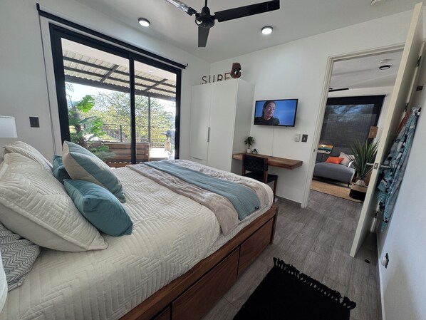 Une chambre à coucher comprenant un lit, un bureau, une télévision et une porte coulissante donnant sur un balcon.