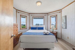 A bedroom with a large bed, wooden walls, and a view of the landscape.