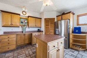 A kitchen with wooden cabinets, a refrigerator, and a coffee maker. - The Final View | 750 ft to the beach | Private Pool, Hot Tub, and Dog Friendly (Corolla)