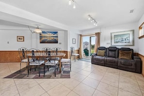 A spacious living area with a dining table, sofa, and artwork on the walls. - The Final View | 750 ft to the beach | Private Pool, Hot Tub, and Dog Friendly (Corolla)
