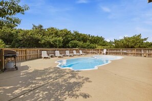A backyard with a swimming pool, lounge chairs, and a barbecue grill.