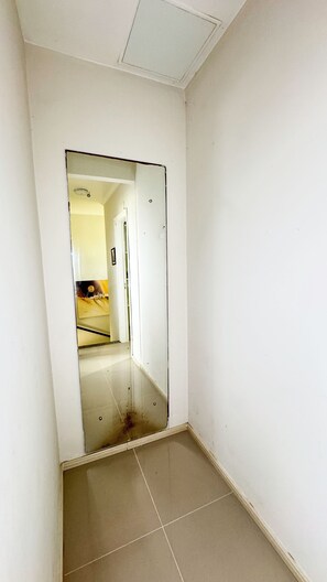 Um corredor estreito com um espelho refletindo um quarto com uma cama e uma porta.