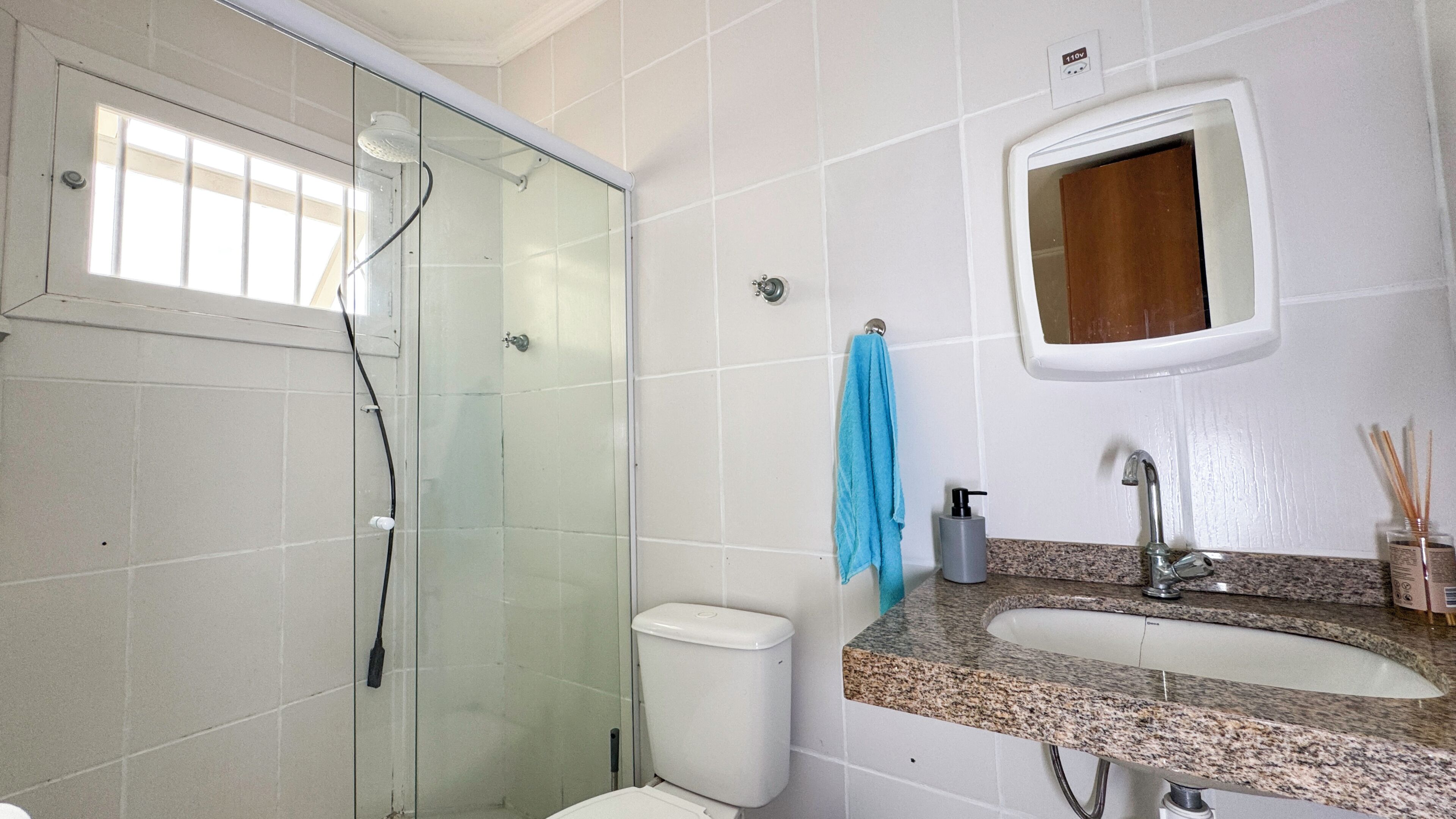 Une salle de bain avec une douche à parois de verre, des toilettes, un lavabo avec un miroir et une serviette accrochée au mur.