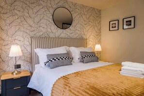 Une chambre d’hôtel avec un lit, deux lampes de chevet, une table de nuit, un miroir et deux tableaux encadrés accrochés au mur.