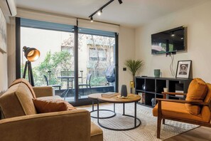 Un salon moderne comprenant un canapé, un fauteuil, une table basse et un téléviseur fixé au mur.