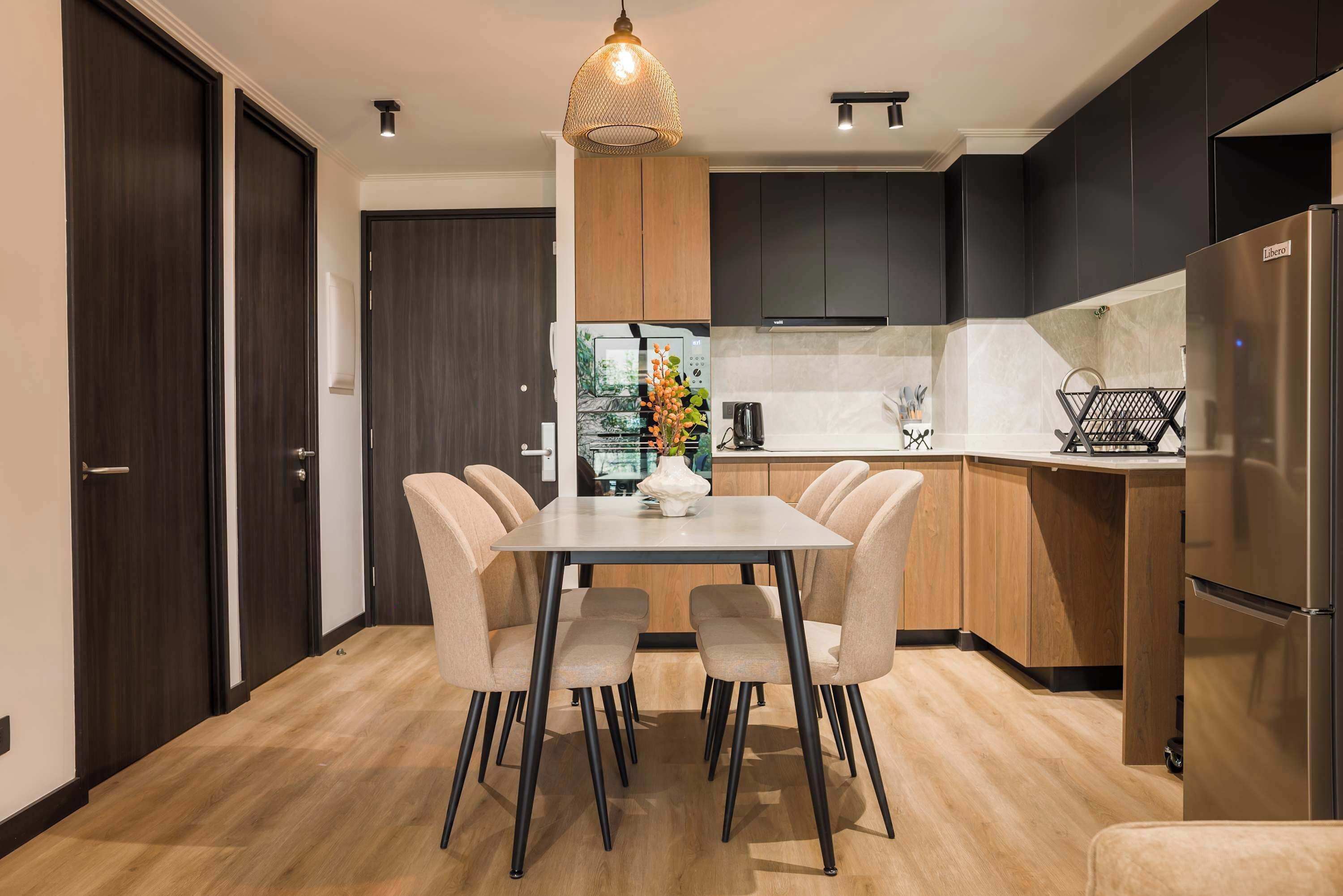A modern kitchen with dark cabinets, a stainless steel refrigerator, and a dining area with a table and chairs.