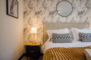 Ein Schlafzimmer mit Bett, Nachttisch, Lampe und einem Spiegel an der Wand.
